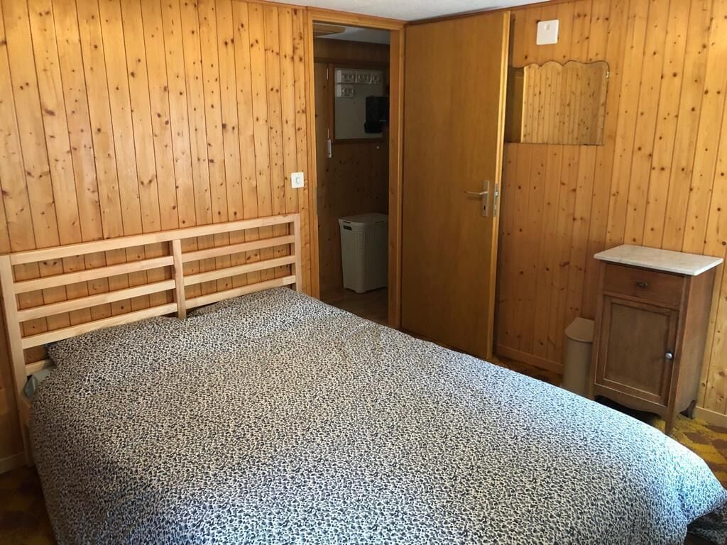 Une chambre à coucher avec une tête de lit en bois, un lit recouvert d’une couvre-lit à motifs, une armoire et un petit meuble.