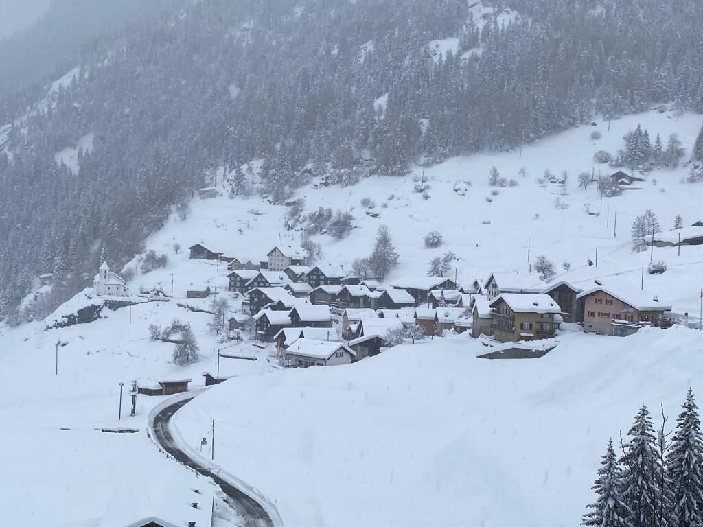 A snow-covered village with traditional houses, a winding road, and a church on a hillside.