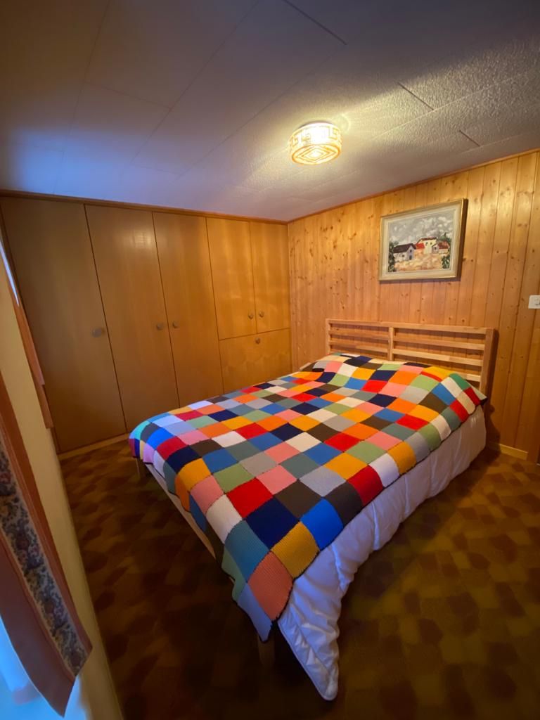 A bedroom with a wooden headboard, a colorful quilt, and a framed picture on the wall.