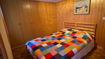 A bedroom with a wooden headboard, a colorful quilt, and a framed picture on the wall.