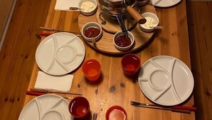 A wooden dining table set with white plates, red bowls, and a central pot. - Chalet del Sole  (Quinto)