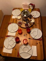 Una mesa de madera con platos blancos, cuencos rojos y una olla en el centro.