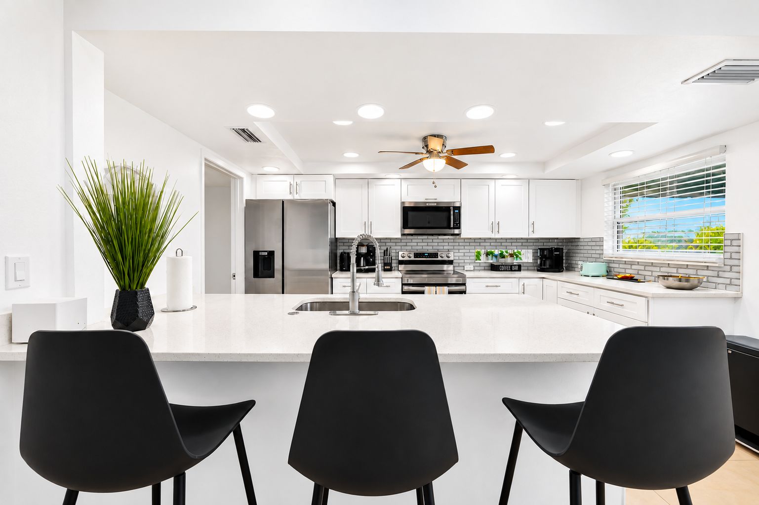 A modern kitchen with a central island, stainless steel appliances, and a ceiling fan.