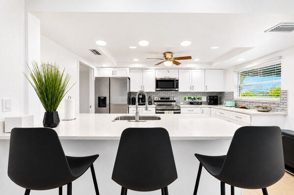 A modern kitchen with a central island, stainless steel appliances, and a ceiling fan.