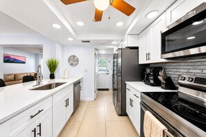 A modern kitchen with white cabinetry, stainless steel appliances, and a ceiling fan.