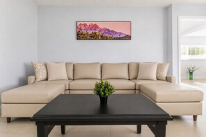 Una sala de estar moderna con un sofá seccional color beige, una mesa de centro negra y un cuadro con un paisaje en la pared.