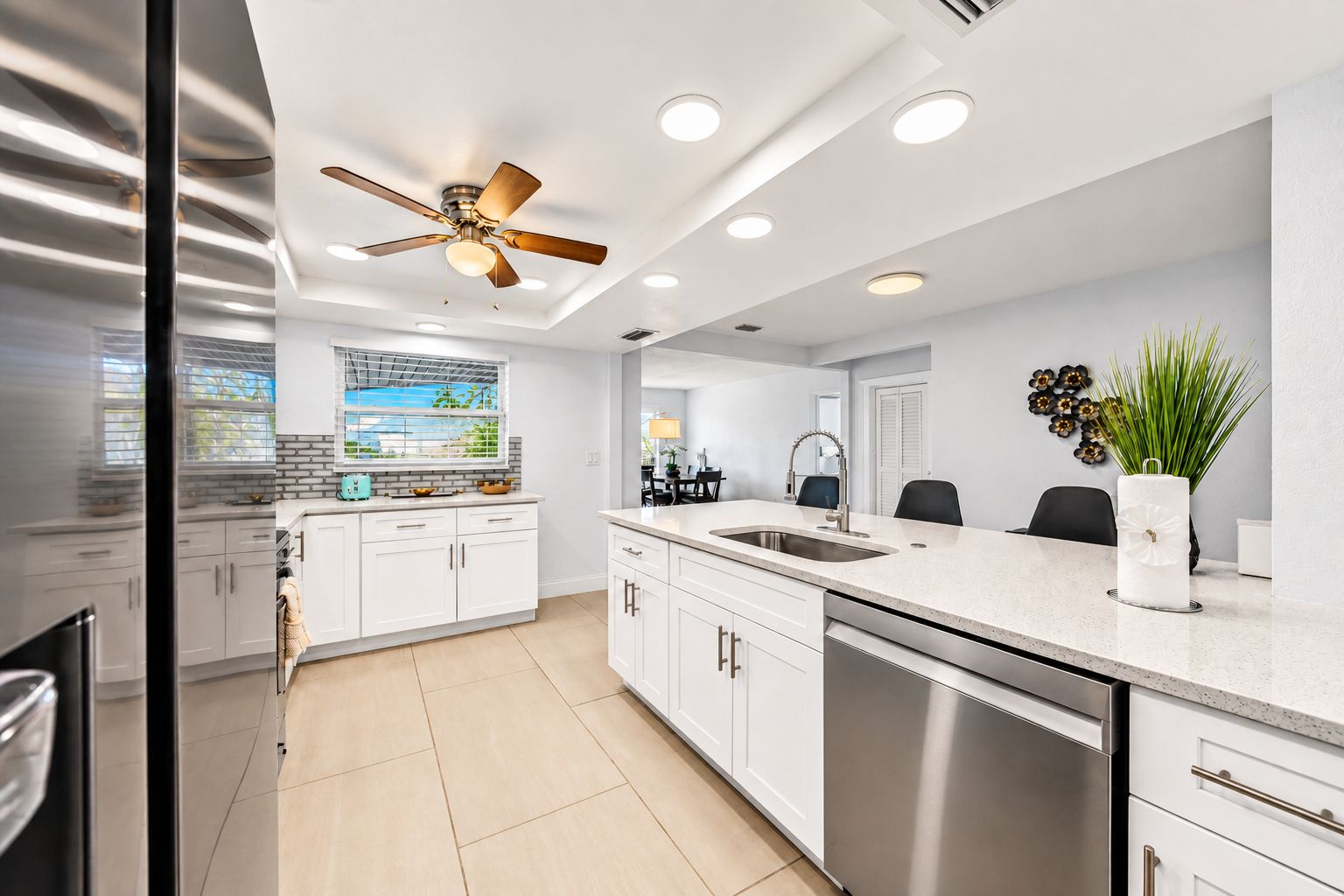 A modern kitchen with white cabinets, a stainless steel dishwasher, and a ceiling fan.