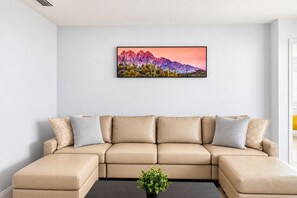 Ein Wohnzimmer mit einem beigefarbenen Ecksofa, einem Couchtisch und einem gerahmten Landschaftsbild an der Wand.