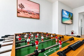 A foosball table in a room with a desert landscape painting and a beach scene painting on the walls.