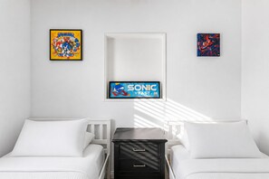 Habitación de hotel con dos camas, una mesita de noche y un televisor de pared mostrando a Sonic el Erizo.