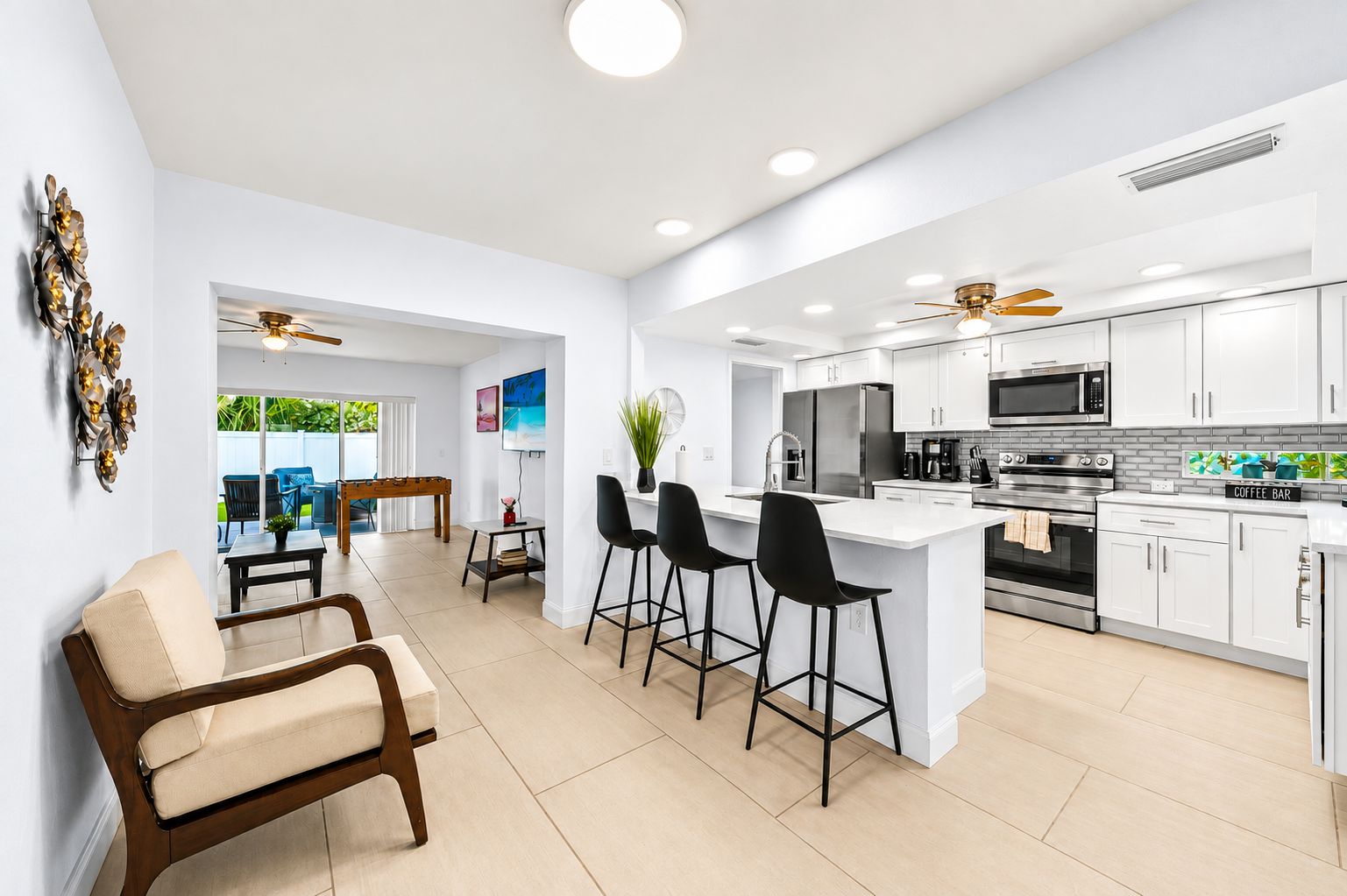 Una cocina moderna con armarios blancos, una isla central con taburetes de bar, un letrero de cafetería y una zona de comedor con mesa y sillas.