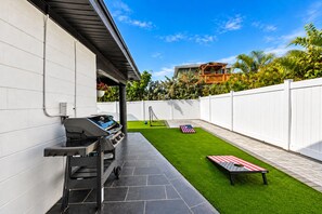 Ein Garten mit Kunstgrasanlage, Grill und weißem Zaun.