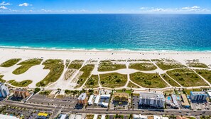An aerial view of a coastal area with a beach, roads, and buildings.