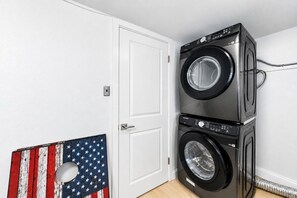 Ein Waschraum mit zwei übereinandergestapelten, frontgeladenen Waschmaschinen, einer weißen Tür und einer an der Wand befestigten Dekoration mit der amerikanischen Flagge.