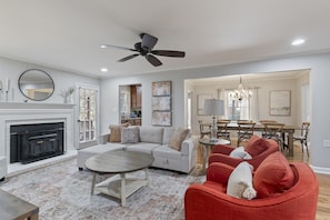 A living room with a fireplace, a ceiling fan, and a dining area with a chandelier. - Marietta GEM 4-bedroom/3 bed - pet friendly -flexible monthly stays  (Marietta)