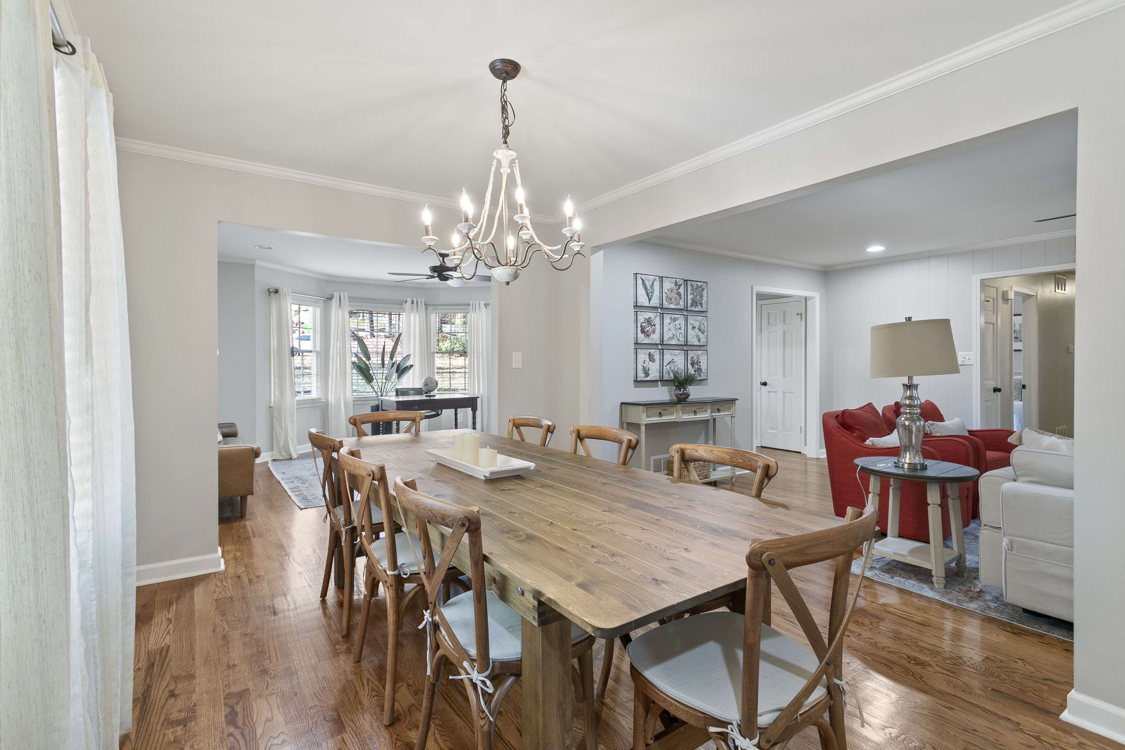 A spacious dining area with a wooden table and chairs, a chandelier, and a red sofa in the background.