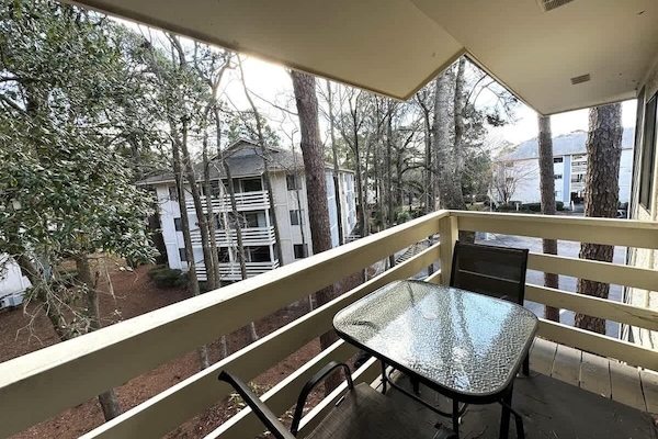 A cozy outdoor retreat with a glass-top table and chairs, in a wooded landscape.
