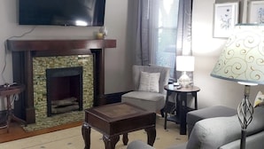 A living room with a fireplace, a television mounted above it, a sofa, a chair, and a lamp. - B-town King and Queen (Bloomington)