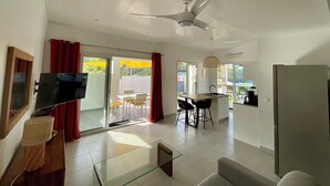 A modern living room with a flat-screen TV, a glass coffee table, and a ceiling fan. - Appartement vue Mer, Rez-de-chaussée Chaussée, Chez Ti Louis - Grande Anse (Les Anses-d'Arlet)