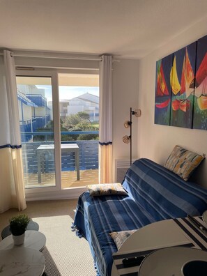 Relax in this inviting space with a sofa, small table, and potted plant, surrounded by a beautiful sailboat painting.