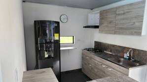 A compact kitchen with a black refrigerator, a stove, a sink, and a clock on the wall. - Quaint Villa in Villavicencio. Connect with nature without compromising comfort (Villavicencio)
