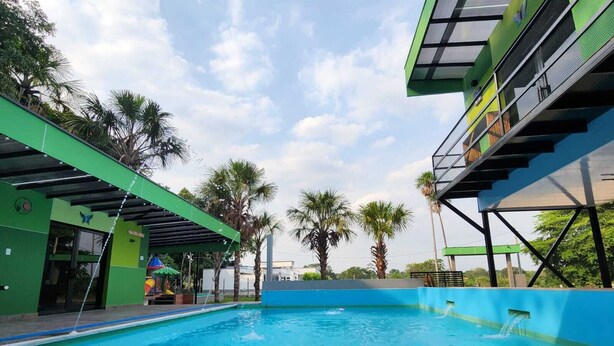 A swimming pool with a clear blue water, surrounded by palm trees and a green building with a covered area. - Quaint Villa in Villavicencio. Connect with nature without compromising comfort (Villavicencio)