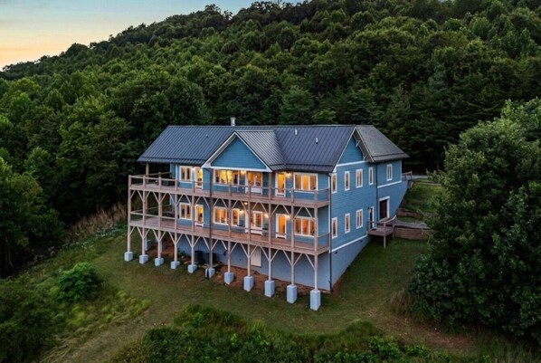 A large, two-story house with a balcony, surrounded by dense forest.