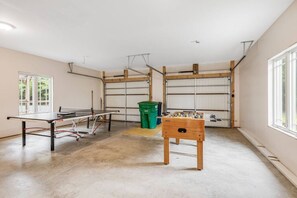 A room with a ping pong table, a foosball table, and a window providing natural light.