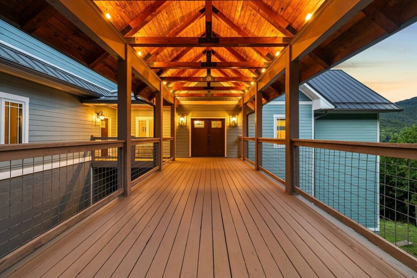 A covered wooden deck with a view of a house and mountains in the background.