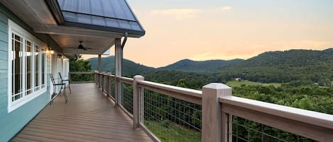 A wooden deck with a metal railing, overlooking a forested landscape.
