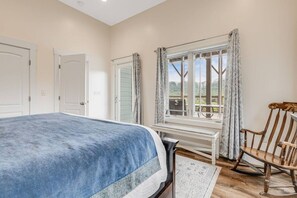 A bedroom with a bed, a desk, a chair, and a window with curtains.