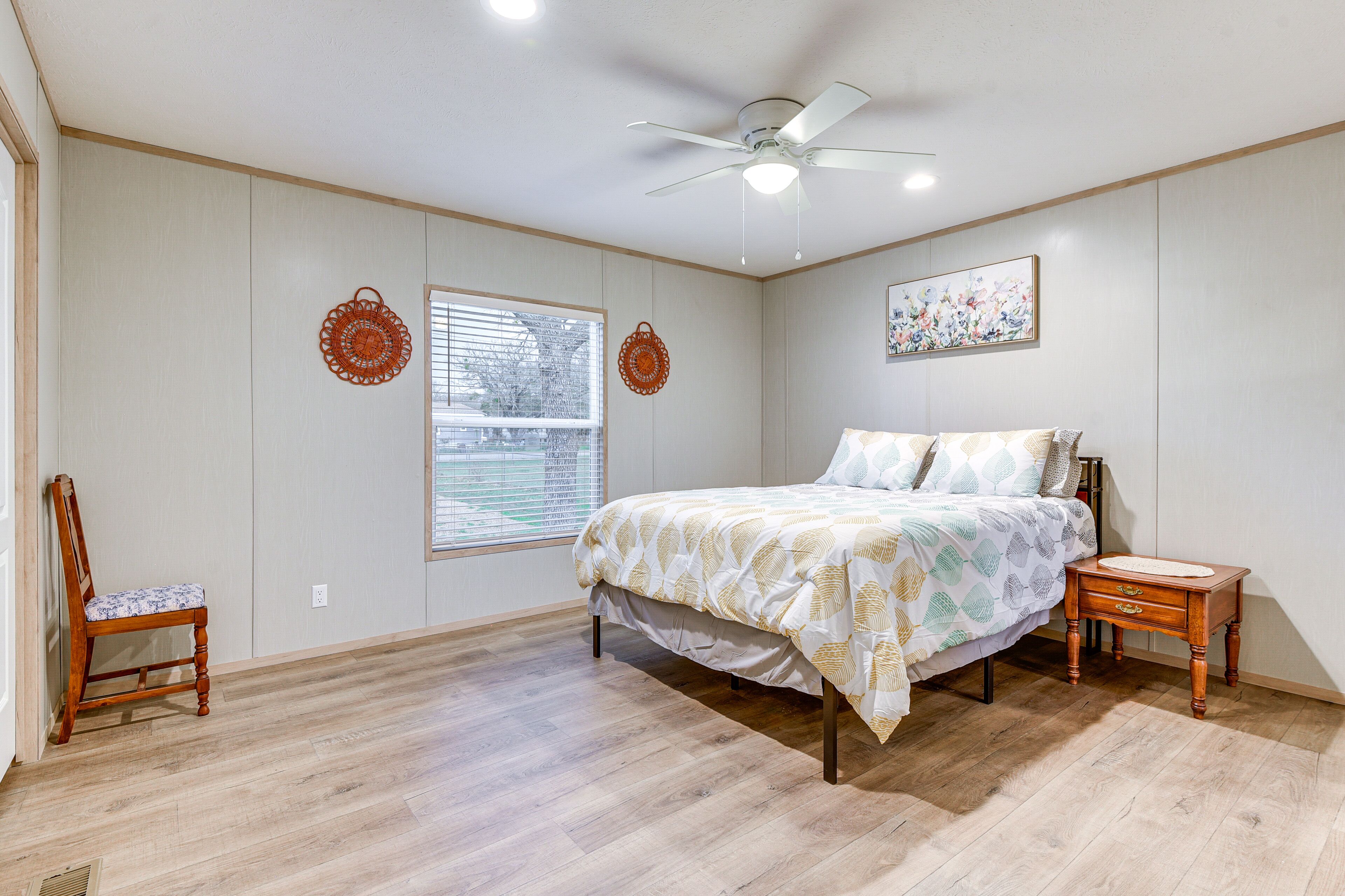 A bedroom with a bed, a chair, a nightstand, a ceiling fan, and a window with blinds.