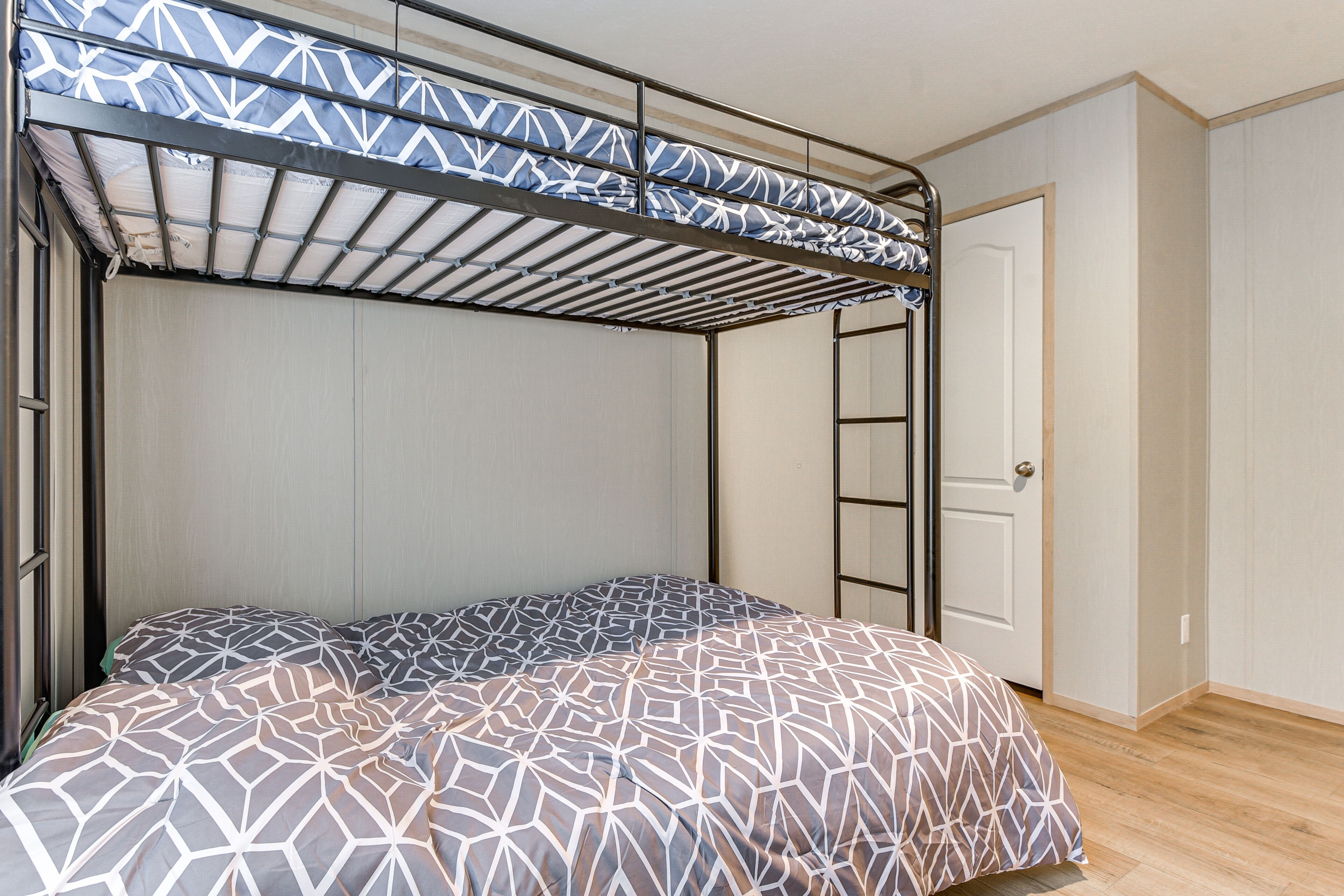 A bunk bed with a geometric-patterned bedspread, a metal ladder, and a door to the right.
