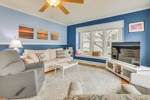A living room with a sofa, armchair, coffee table, TV, and artwork on the walls. - Ludington Home w/ 6 Bicycles < 1 Mi to Beach! (Ludington)