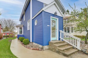 Une maison à deux étages, avec une façade bleue, une porte d’entrée blanche et un petit porche doté de quelques marches.