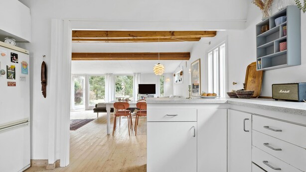 A modern kitchen with white cabinetry, a wooden ceiling, and a dining area with a table and chairs.