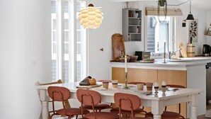 A modern kitchen with white cabinetry, a central island, and a dining area with a white table and red chairs.