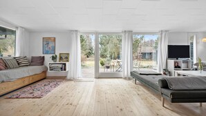 A spacious living room with a large window, a sofa, a TV, and a bookshelf.