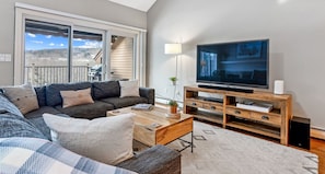 A living room with a sofa, coffee table, TV, and a balcony with a view.