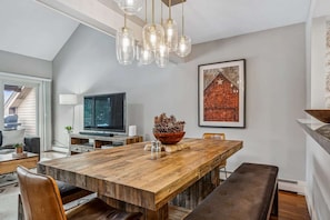 A dining area with a wooden table, chairs, a television, and a framed picture on the wall.