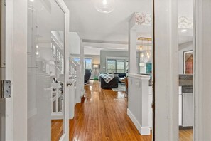 Un couloir doté d’un plancher en bois, de murs blancs et offrant une vue sur un espace de vie comprenant un canapé et une table à manger.