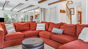 Een ruime woonkamer met een grote hoekbank, een rond hocker en een houten trap.