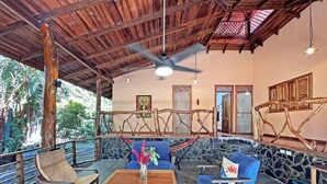 A covered outdoor seating area with wooden furniture, stone walls, and a ceiling fan. - Casa & Casita Miel - 3 Bed Jungle Oasis W/ Pool (Puerto Viejo de Talamanca)