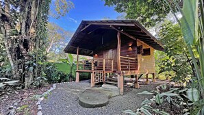 A wooden cabin with a sloped roof, surrounded by dense foliage and a gravel path. - Casa & Casita Miel - 3 Bed Jungle Oasis W/ Pool (Puerto Viejo de Talamanca)