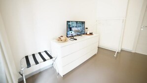 A white room with a TV on a dresser, a small stool, and a radiator. - Crusco Room - Camera con letto matrimoniale e un divano letto (Matera)