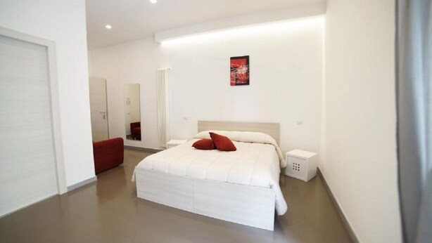 A modern bedroom with a large bed, a bedside table, a red bench, and a wall-mounted artwork. - Crusco Room - Camera con letto matrimoniale e un divano letto (Matera)