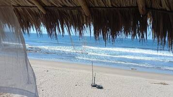 Une scène de plage avec une structure à toit de chaume, une plage de sable et des vagues de l’océan.