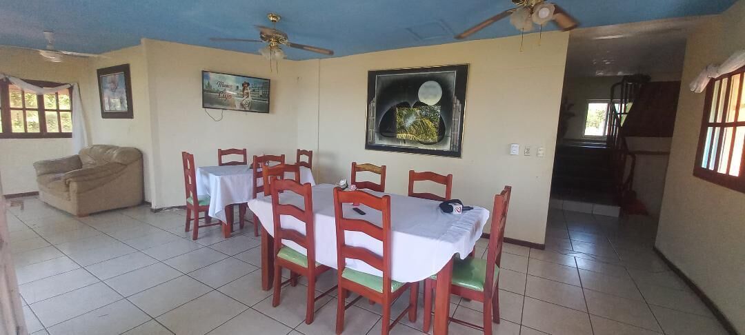 A dining area with a table set for six, surrounded by wooden chairs. There is a sofa in the corner and a ceiling fan above.
