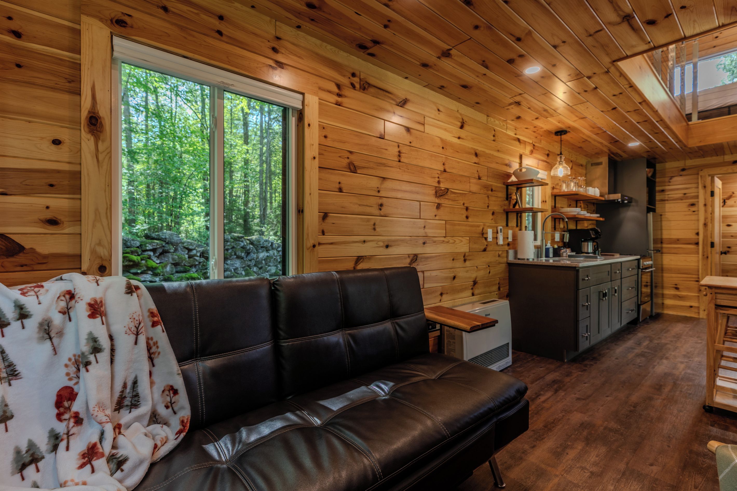 Een chaletinterieur met een leren bank, houten wanden, een keukenhoek en een groot raam.