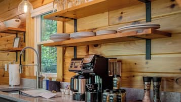 Interior de madeira com máquina de café, prateleiras com pratos e janela com vista para árvores.